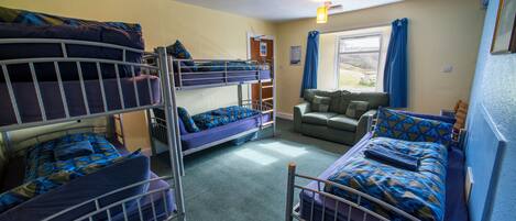 A dormitory room with bunk beds, a sofa, and a window with curtains.