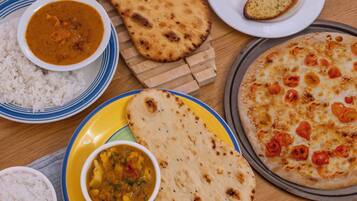 A variety of dishes including rice, curry, flatbread, and pizza on a wooden table.