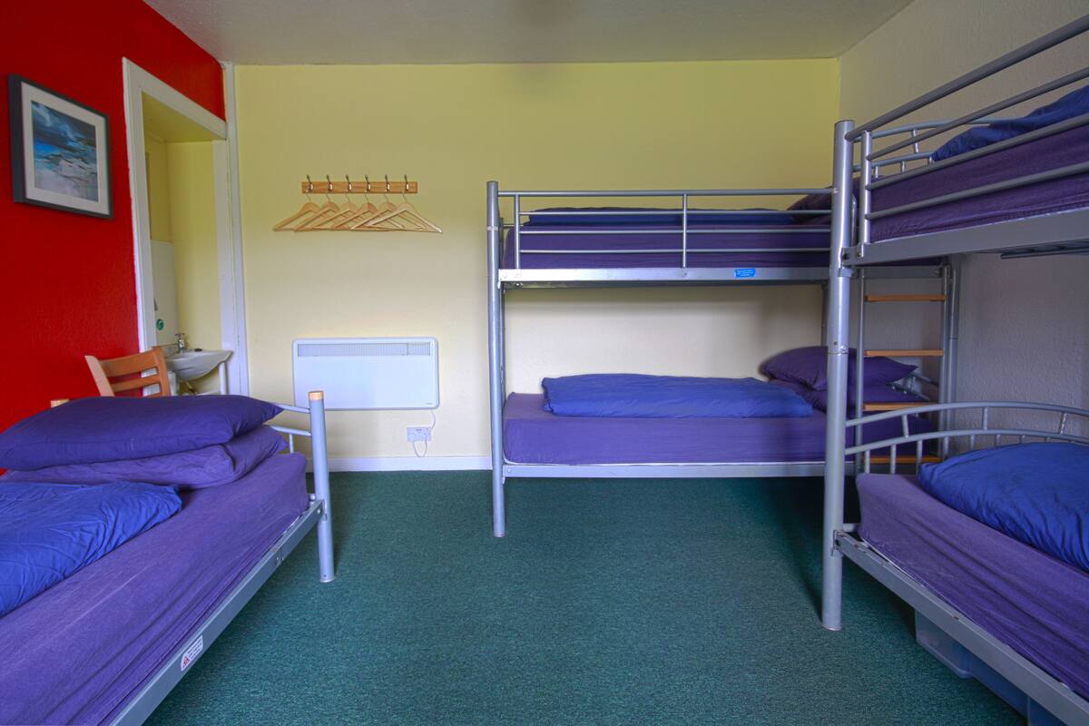 Ein Schlafsaalzimmer mit Etagenbetten, einem Heizkörper, einem Stuhl und einem Kleiderhaken.