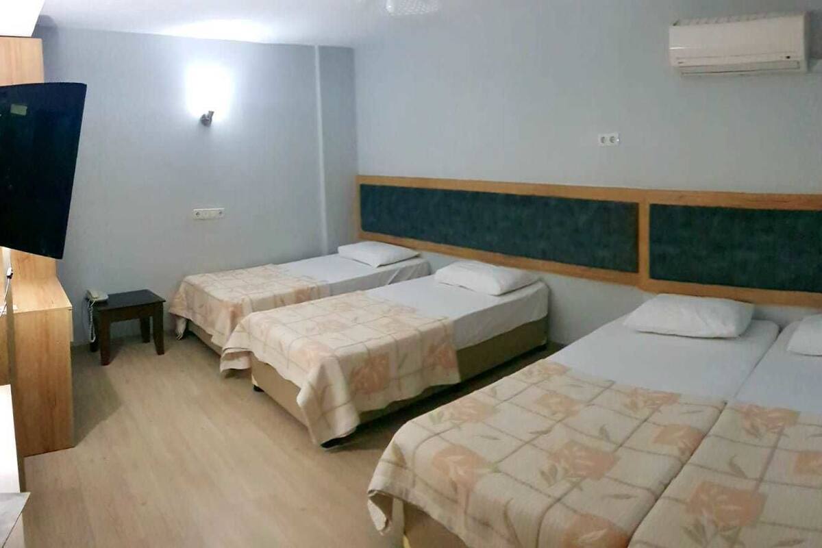 A hotel room with three single beds, a wooden desk, a television, and an air conditioning unit.