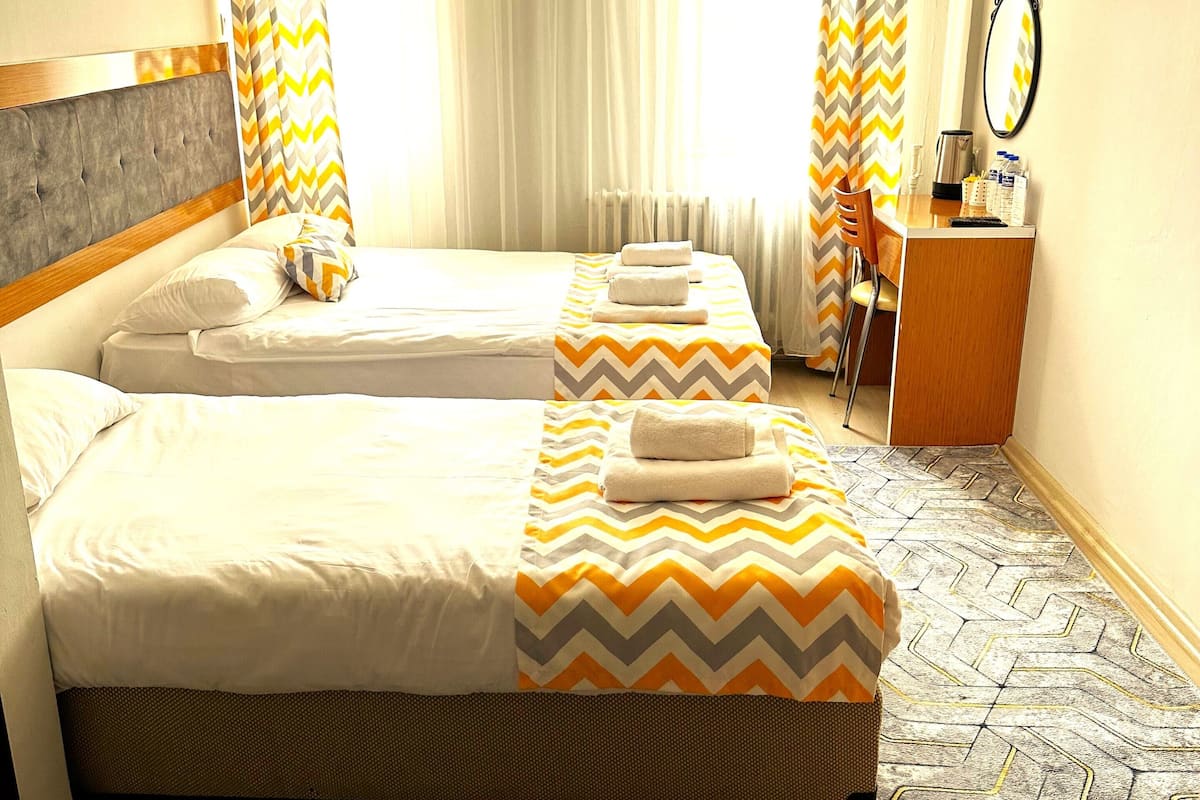 A hotel room with two beds, a desk, a chair, a mirror, and a TV.