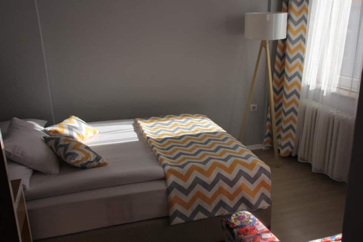 A bedroom with a bed, pillows, a bedside lamp, and curtains.