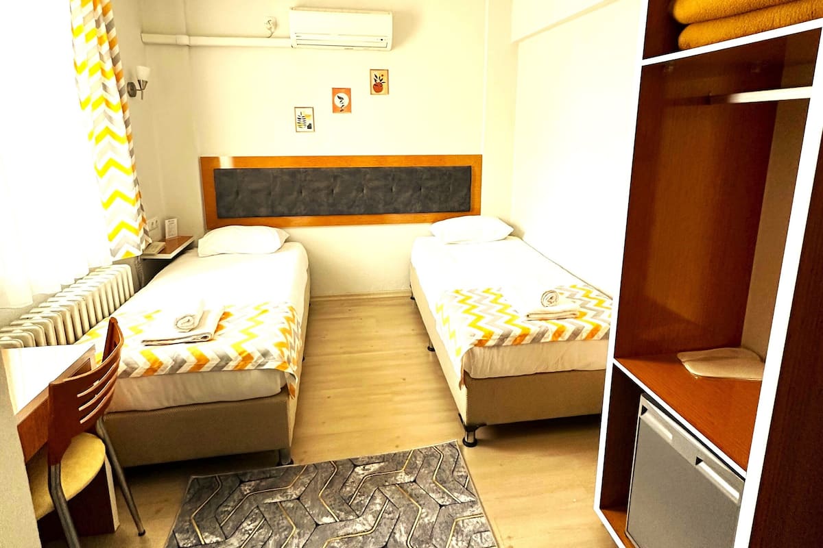 A hotel room with two beds, a desk, a chair, a wardrobe, and a radiator.