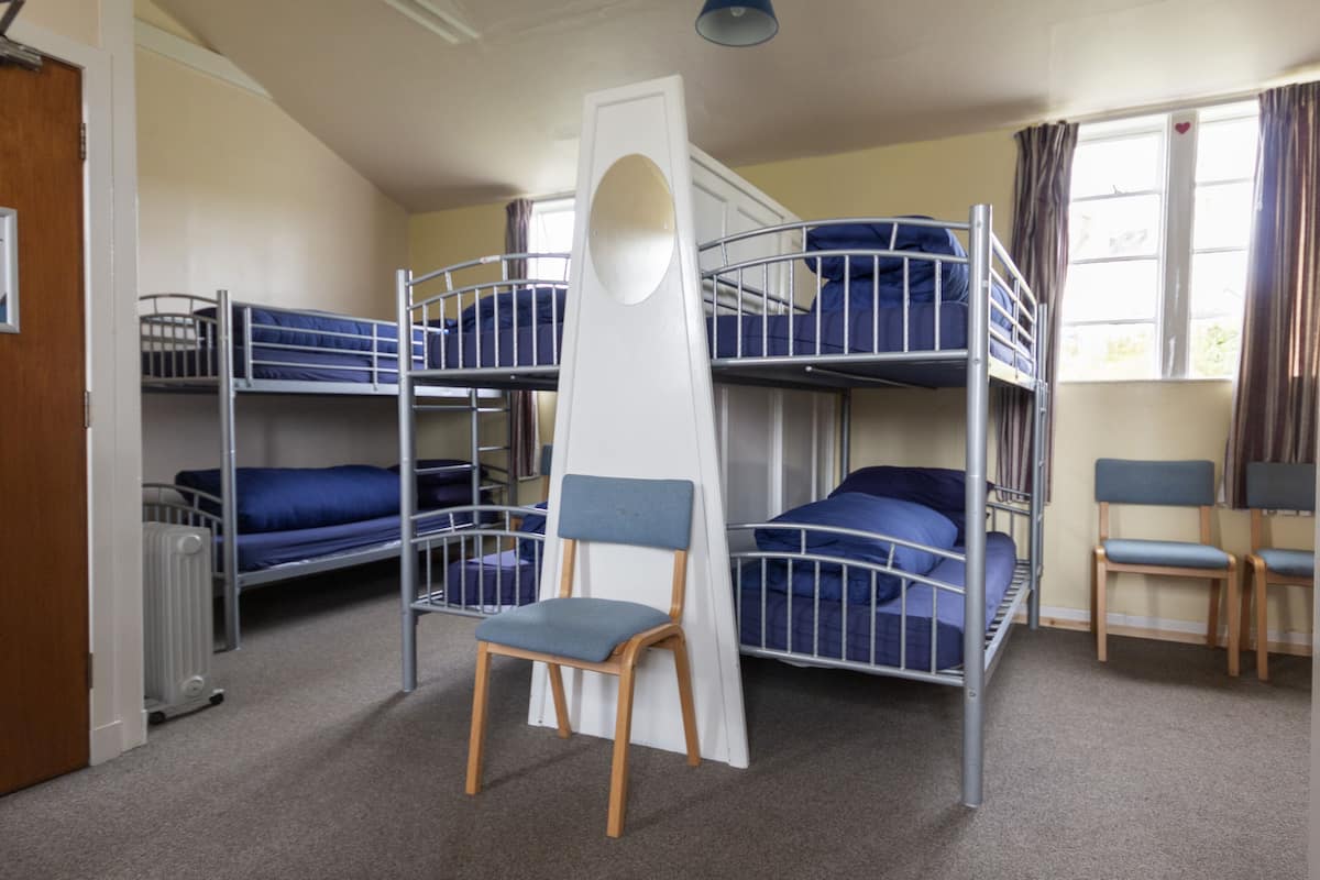 A dormitory room with bunk beds, a chair, and a radiator.
