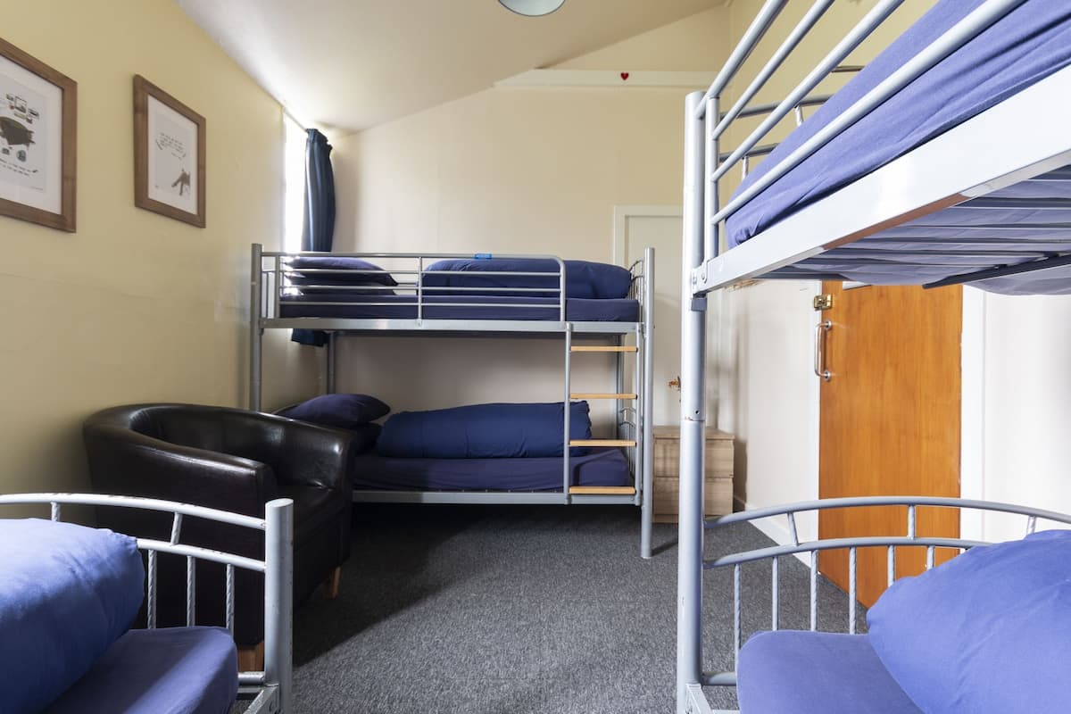 A dormitory room with bunk beds, a desk, and a chair.