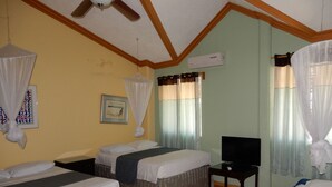 Una camera d'albergo con due letti, una televisione, un condizionatore e una ventola a soffitto.