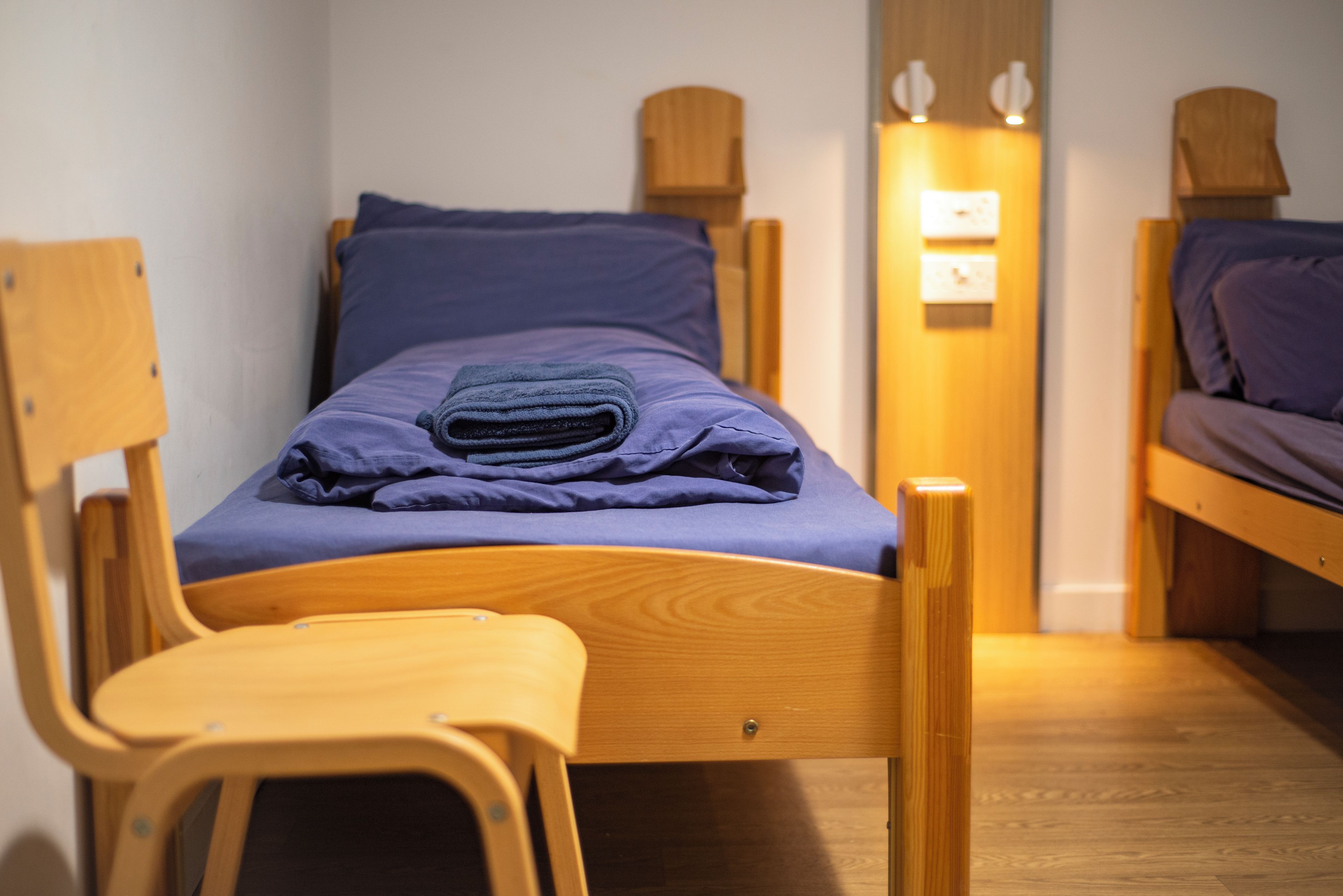 Un lit simple avec un cadre en bois et un matelas bleu, flanqué de deux chaises en bois.