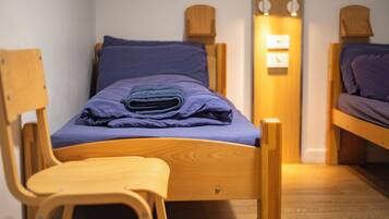Un lit simple avec un cadre en bois et un matelas bleu, flanqué de deux chaises en bois.