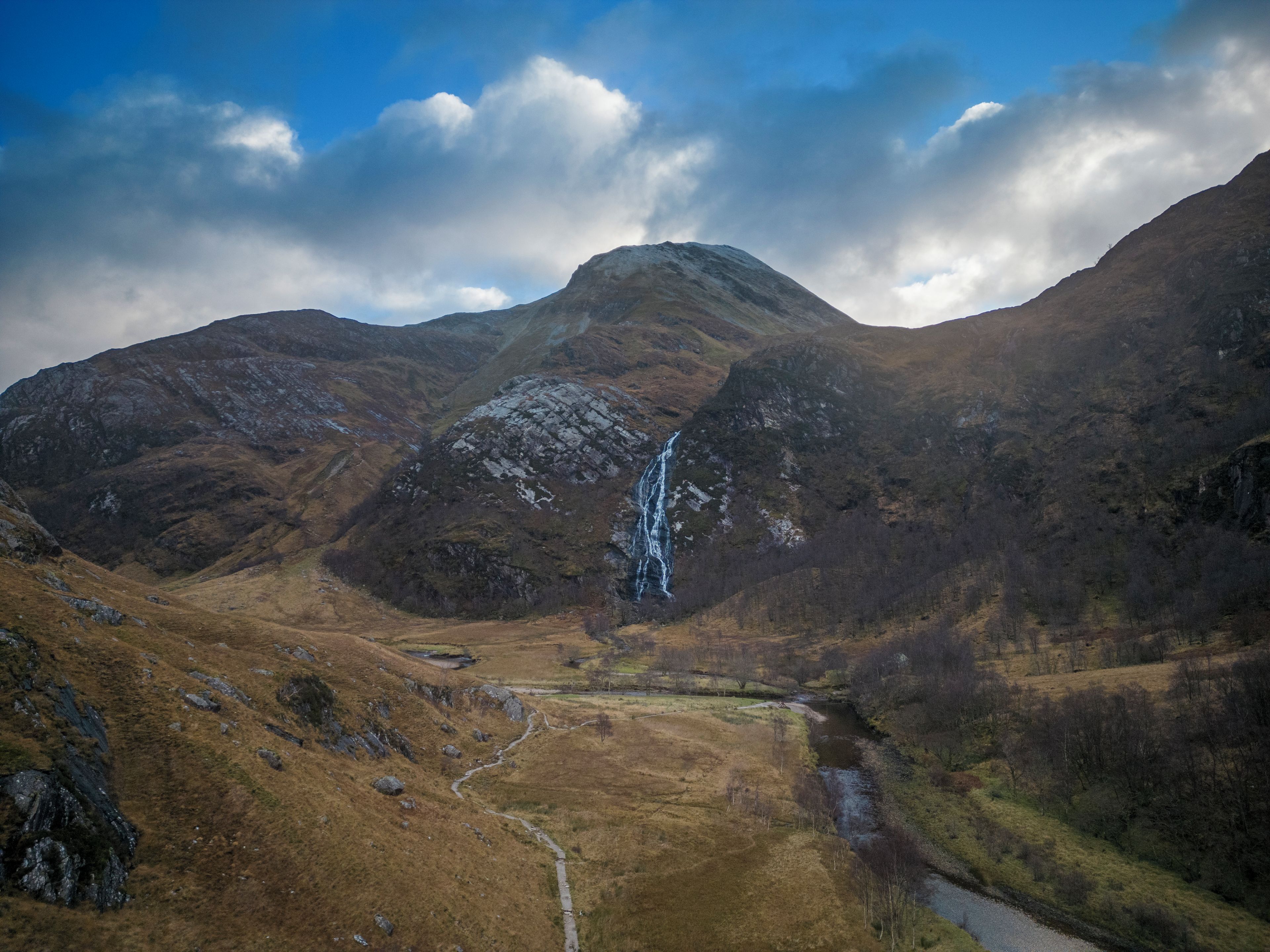 A mountainous landscape with a waterfall, a valley, and a river.