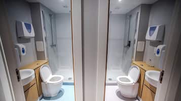 Reflexo de um banheiro moderno com duas sanitárias, pia e chuveiro.