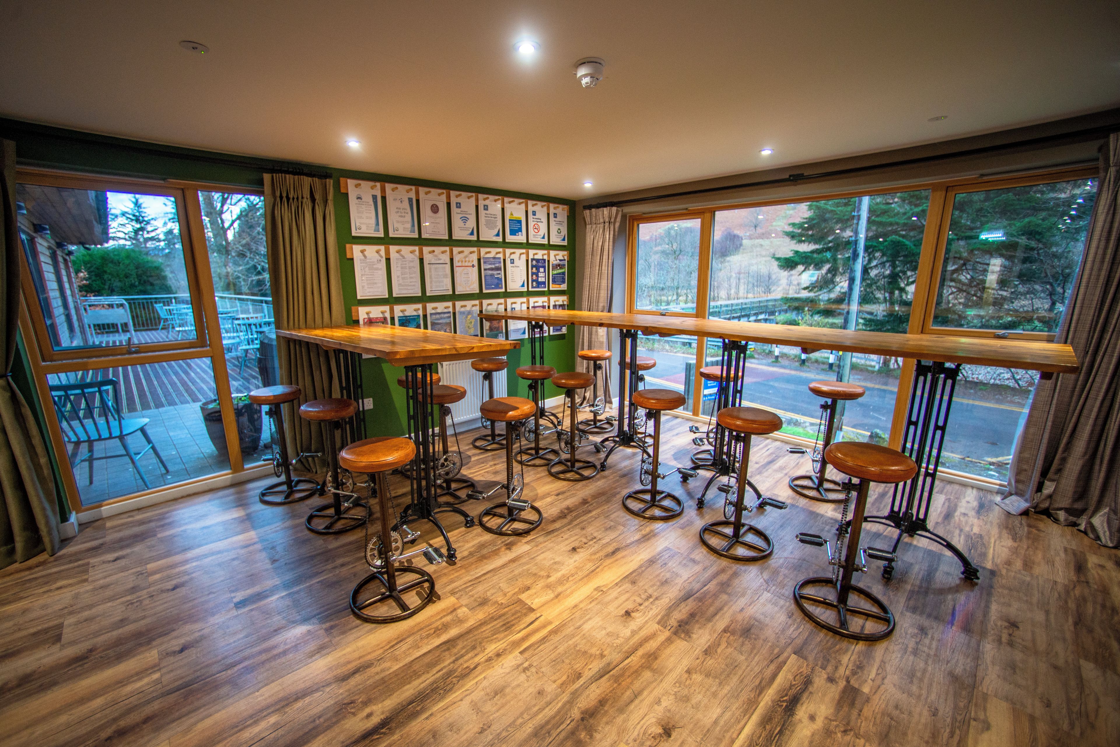 A bar area with stools and a long counter, large windows with a view of trees, and a green wall with informational posters.