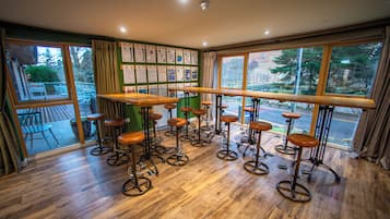 A bar area with stools and a long counter, large windows with a view of trees, and a green wall with informational posters.