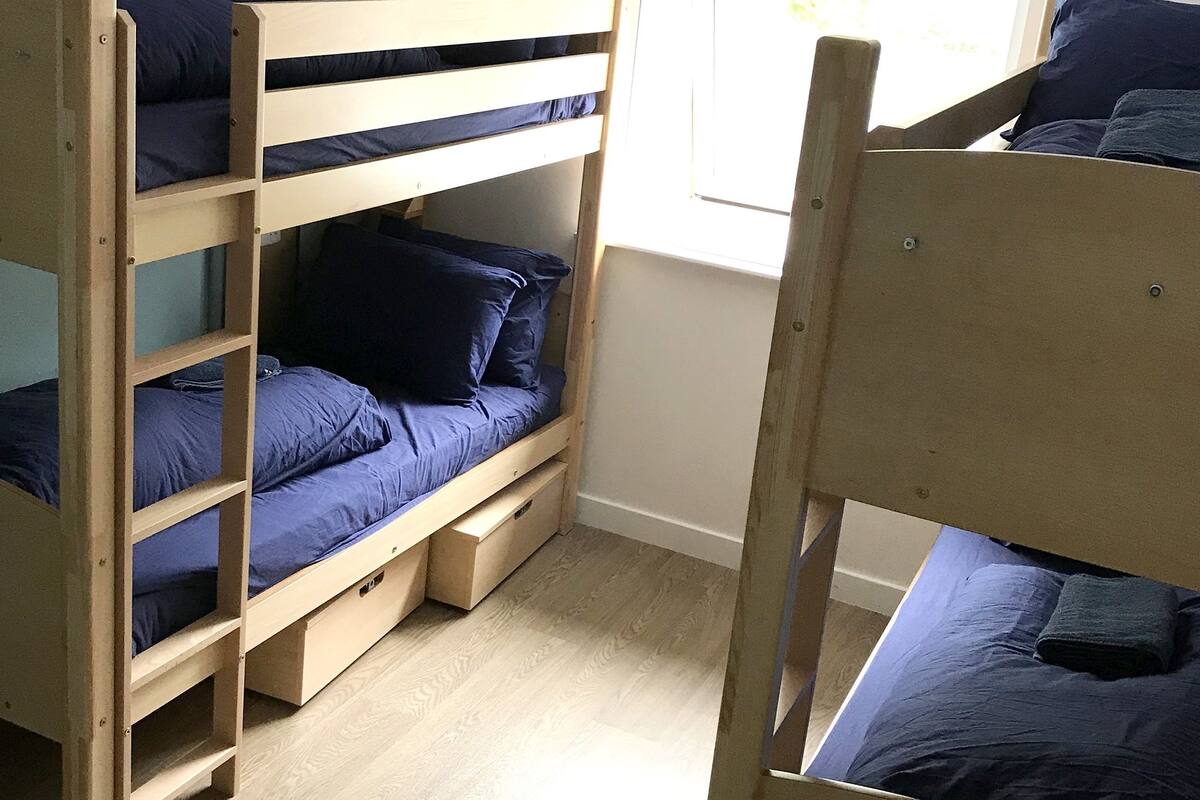A bunk bed room with a window, wooden flooring, and a white wall.