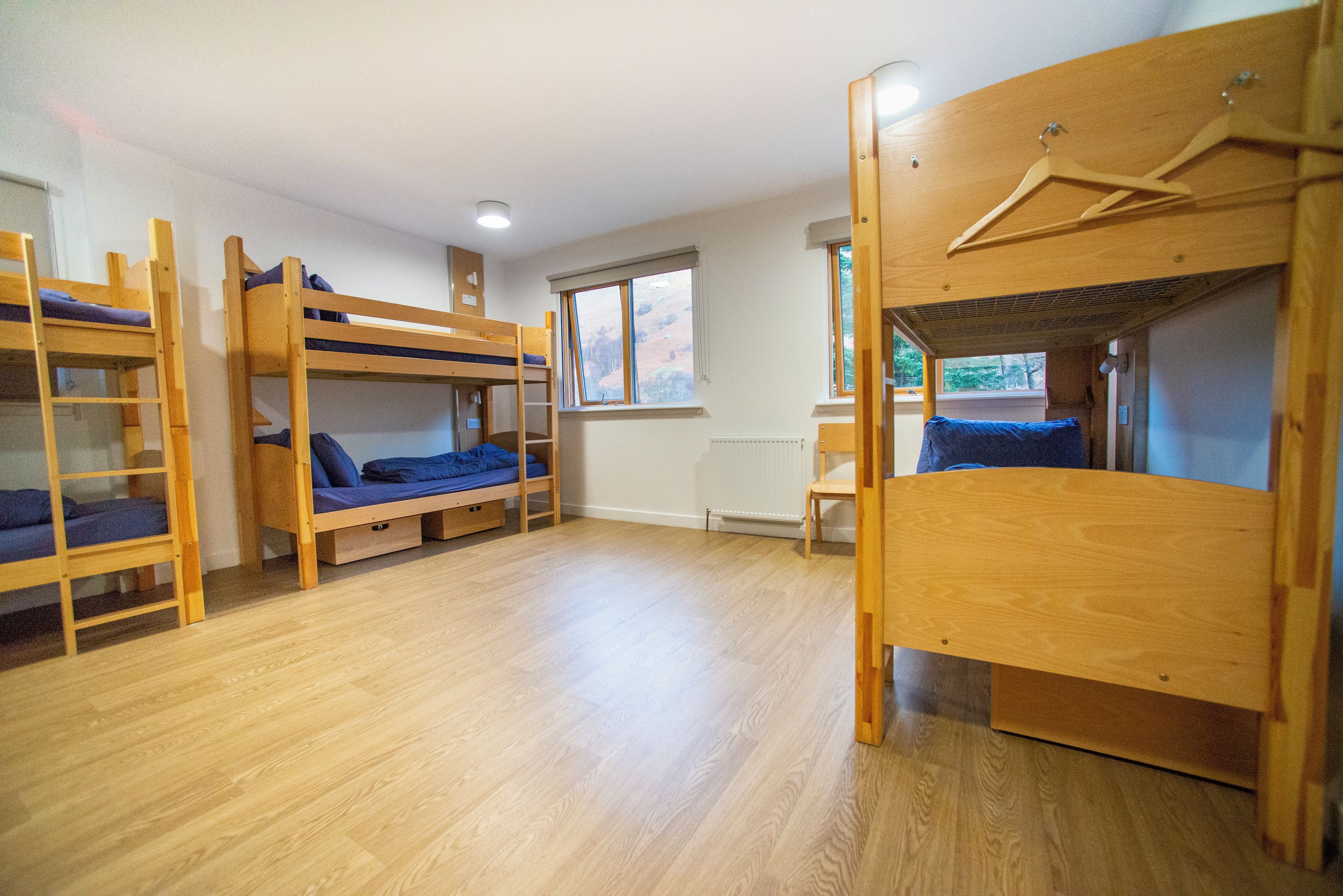 A dormitory room with bunk beds, a radiator, a window, and a wooden chair.