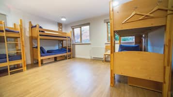 A dormitory room with bunk beds, a radiator, a window, and a wooden chair.