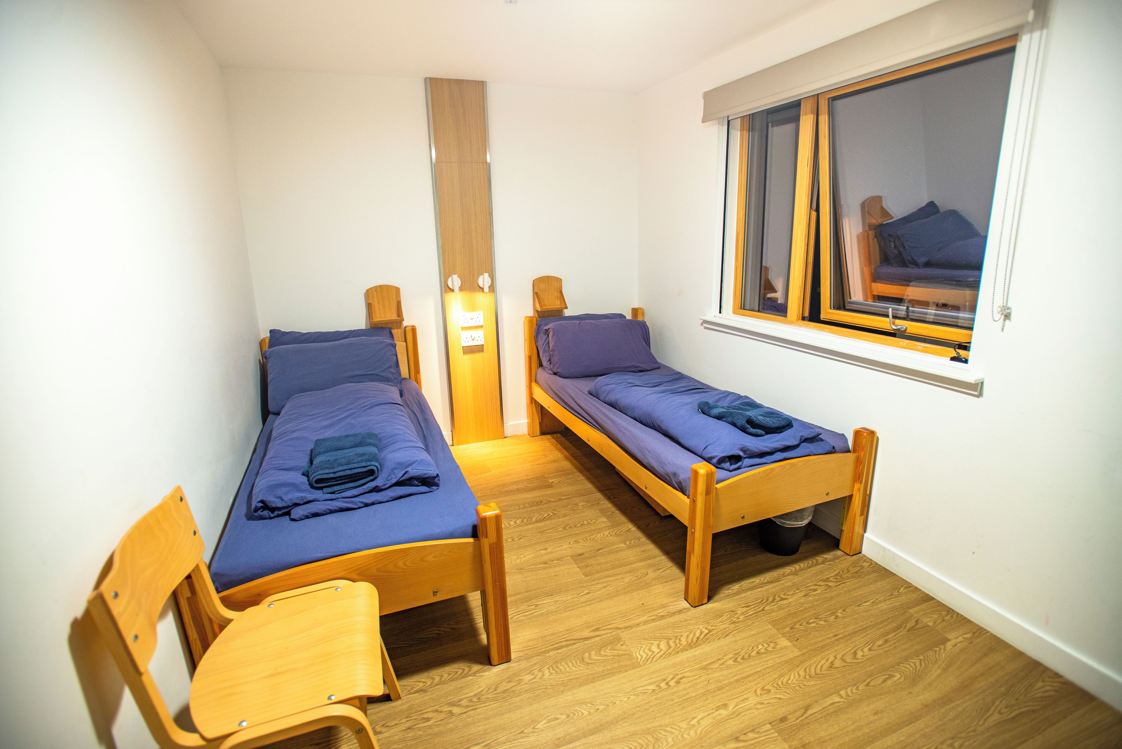 A small, compact room with two wooden beds, a wooden chair, and a window with a view.