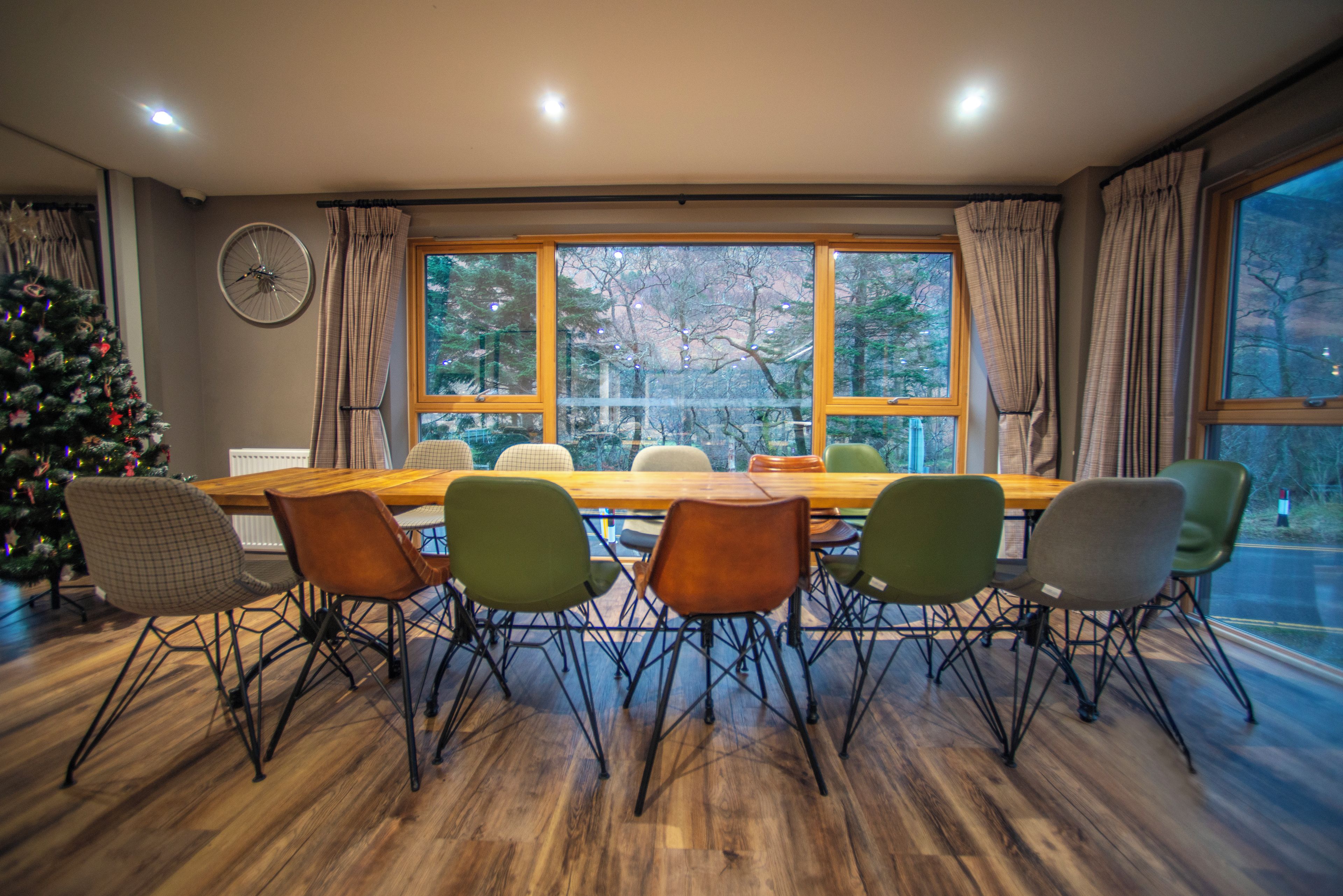 Uma sala de jantar com uma mesa e cadeiras de madeira, uma árvore de Natal e uma janela com cortinas.