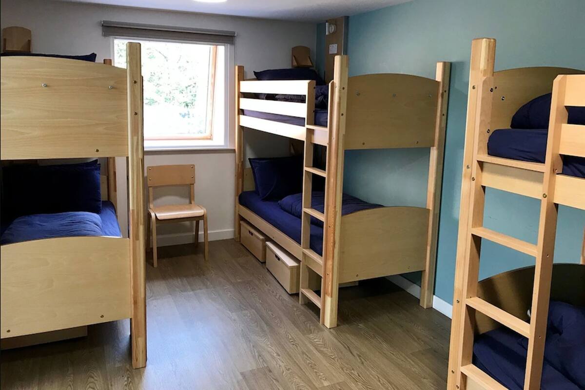 A room with bunk beds, a wooden chair, and a window with blinds.