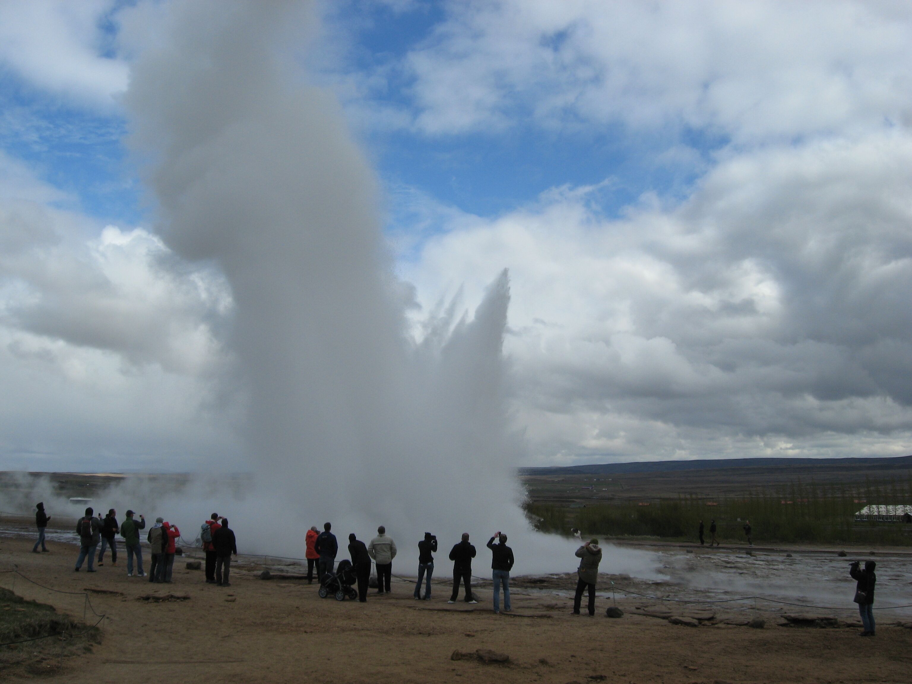 A group of people observing a geyser eruption.