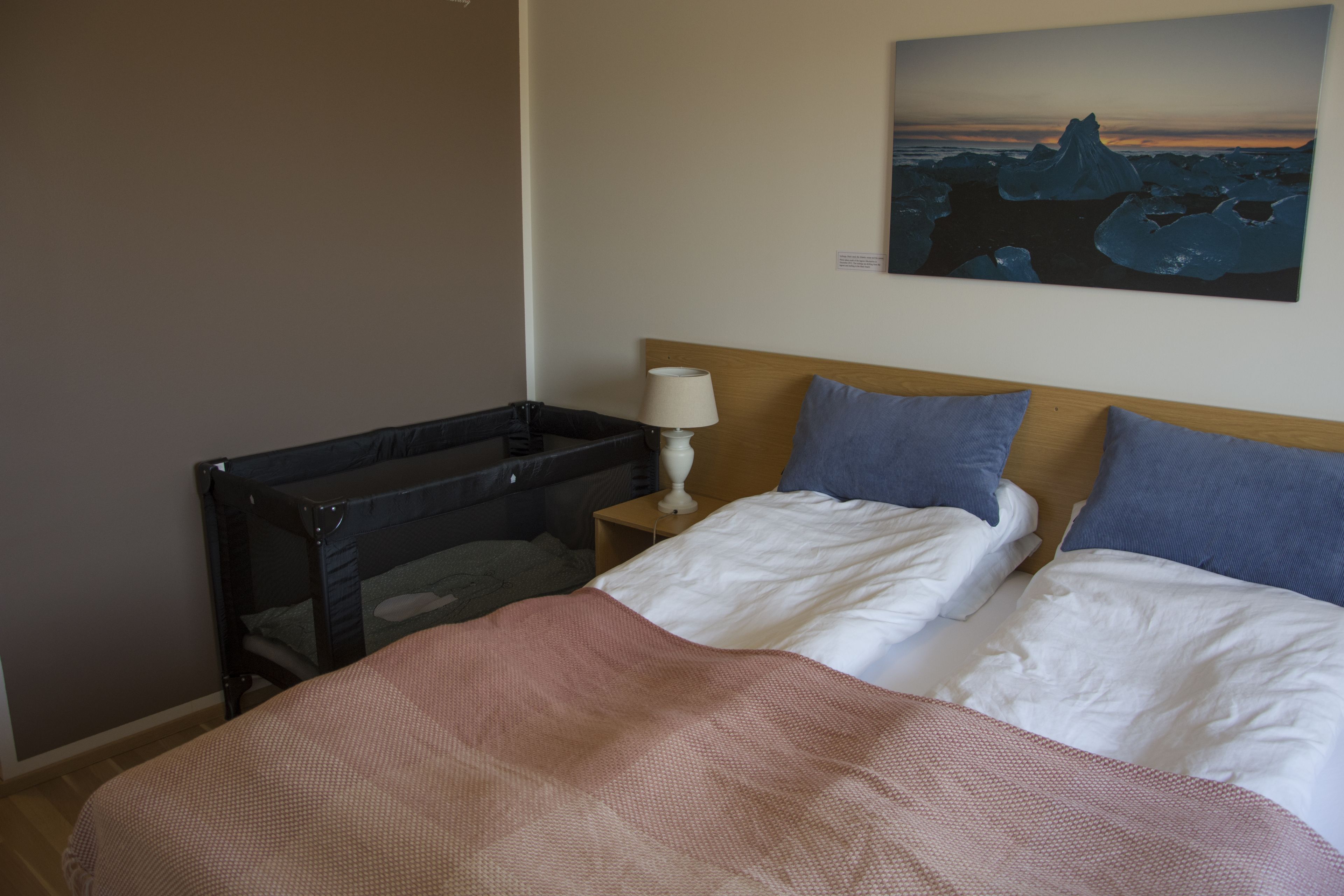 A bedroom with a bed, pillows, a nightstand, a lamp, and a painting of a glacier on the wall.