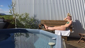 A person relaxing on a wooden bench by a hot tub on a wooden deck. - Lambastadir Guesthouse (Selfoss)