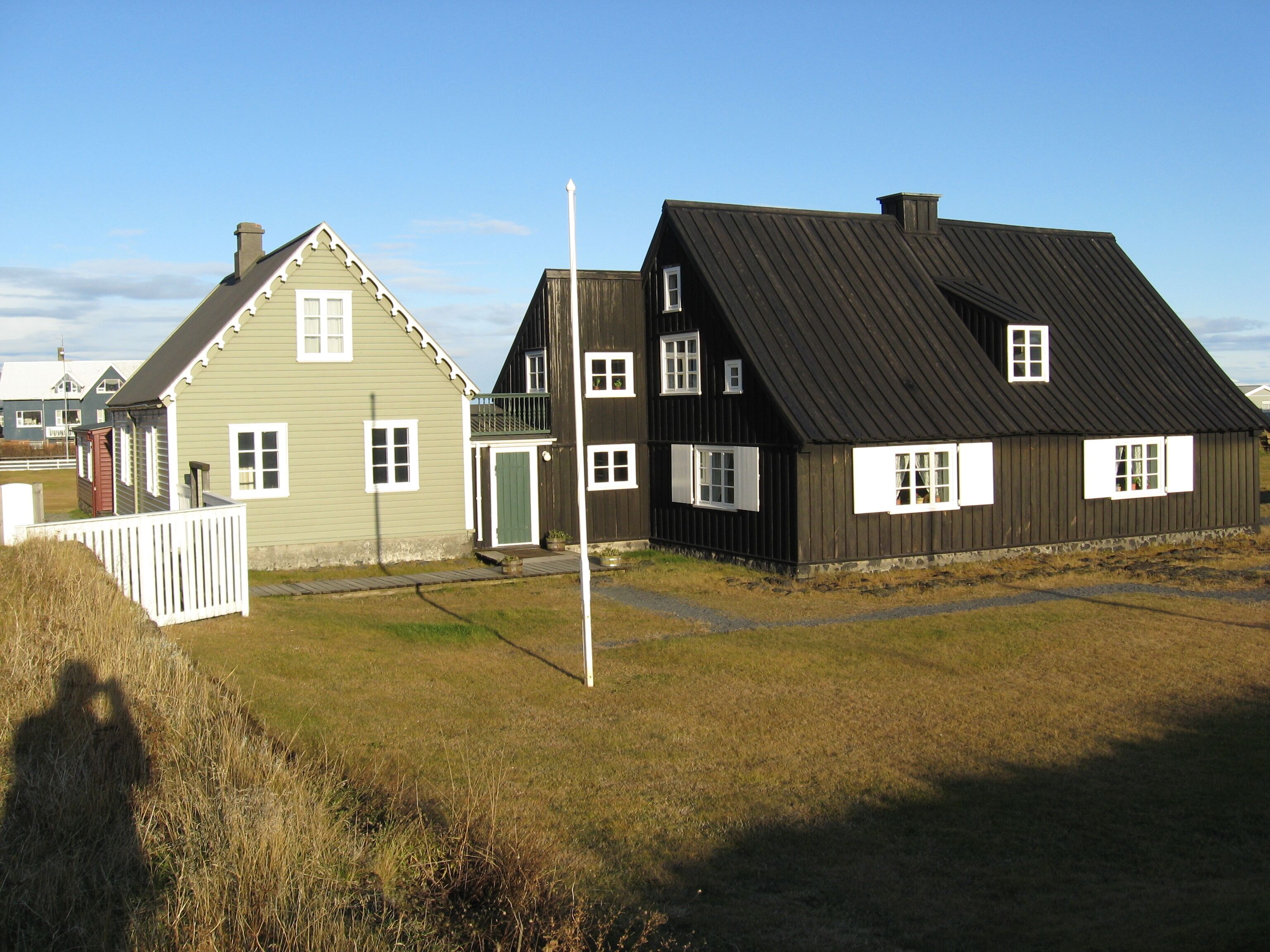 A row of two-story houses with gabled roofs, a wooden fence, and a grassy field.