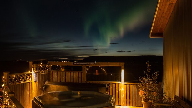A hot tub area with a wooden deck, a covered seating area, and a view of the northern lights. - Lambastadir Guesthouse (Selfoss)