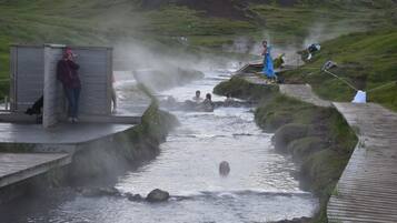 A hot spring area with wooden walkways, a small shelter, and people enjoying the water.
