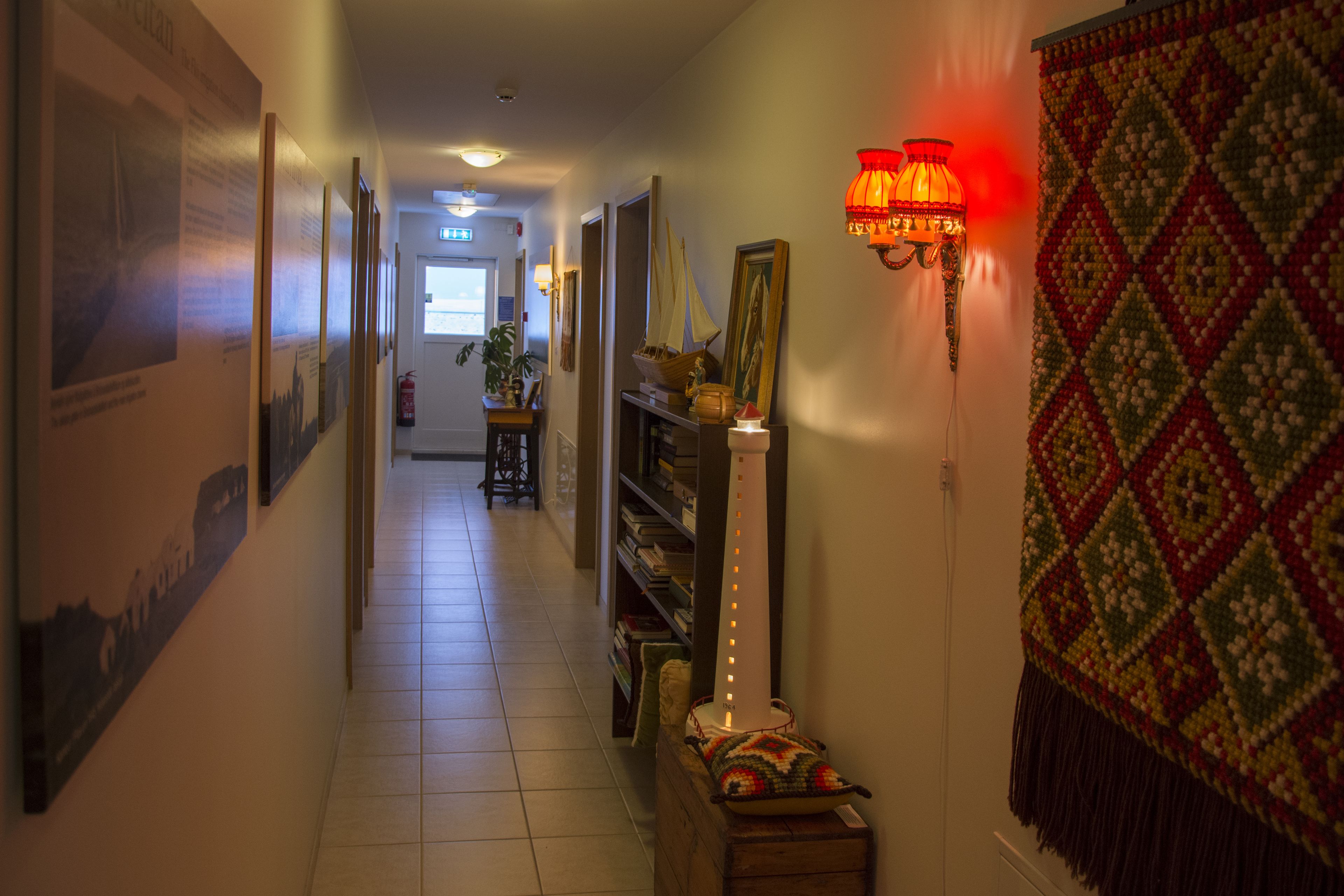 A hallway with framed pictures on the walls, a red decorative lamp, and a patterned rug.