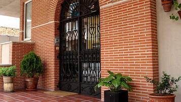 A brick building with a black wrought iron gate, potted plants, and a stone wall.