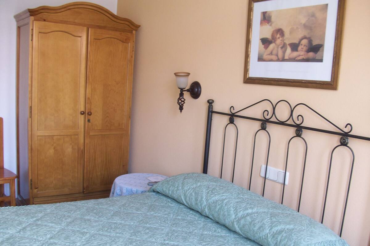 A bedroom with a bed, a wooden wardrobe, a wall-mounted light fixture, and a framed picture.