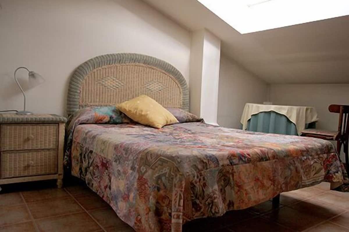 A bedroom with a bed, a bedside table, a lamp, and a chair.