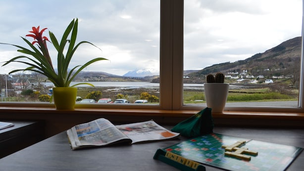 Ein Tisch mit Pflanze, Schale und Spielbrett vor einem Fenster mit Blick auf eine Landschaft mit Bergen und Häusern.