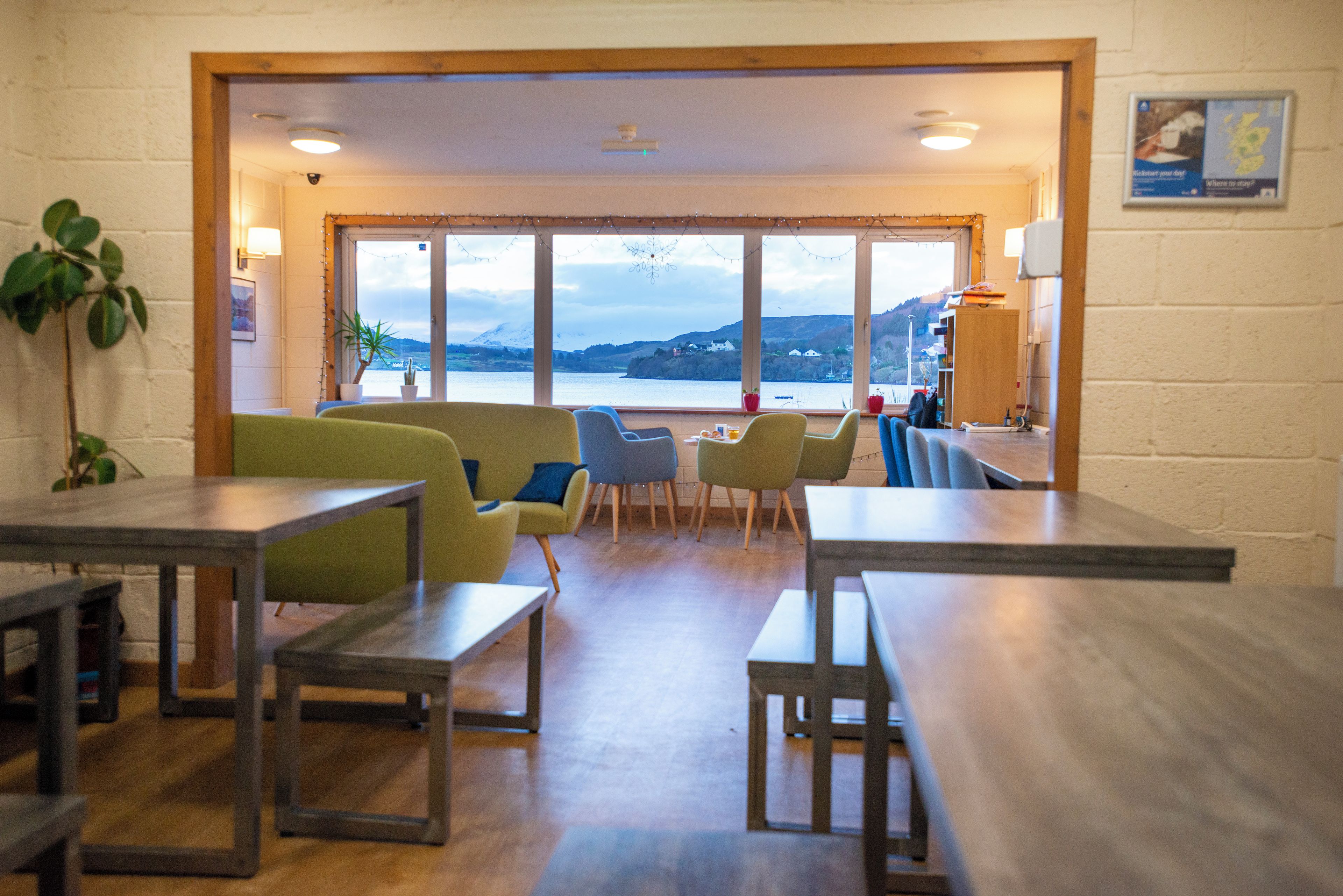 A room with a view of a lake and mountains, furnished with tables and chairs.