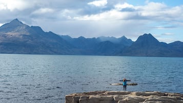 A person standing on a rocky outcrop by a calm lake with mountains in the background.