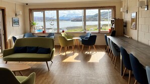 Ein gemütliches Zimmer mit großem Fenster und Blick auf einen See, ausgestattet mit einem grünen Sofa, blauen Stühlen und einem Holztisch.