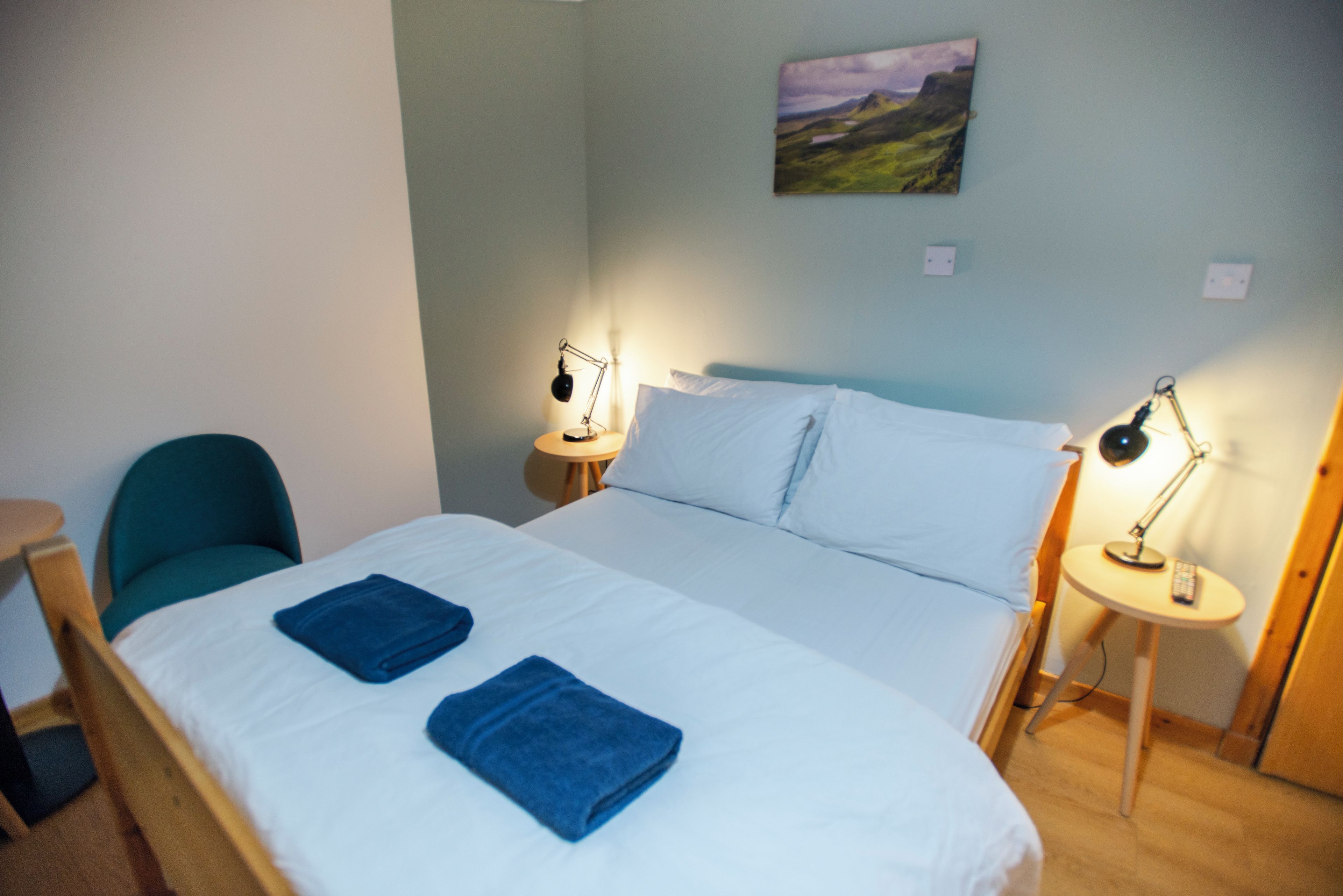 Una habitación de hotel con una cama, dos lámparas de noche, una silla y un cuadro en la pared.