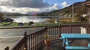 Ein malerischer Blick von einem Balkon auf einen See mit Booten, geparkten Autos und Häusern im Hintergrund.