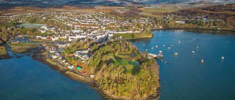 An aerial view of a coastal town with a harbor, boats, and a mountainous backdrop.