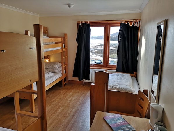 A room with bunk beds, a table with a book, and a window with curtains. - Portree Youth Hostel (Portree)