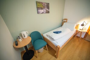 A small, tidy room with a single bed, a chair, a small table, a kettle, and a lamp. - Portree Youth Hostel (Portree)