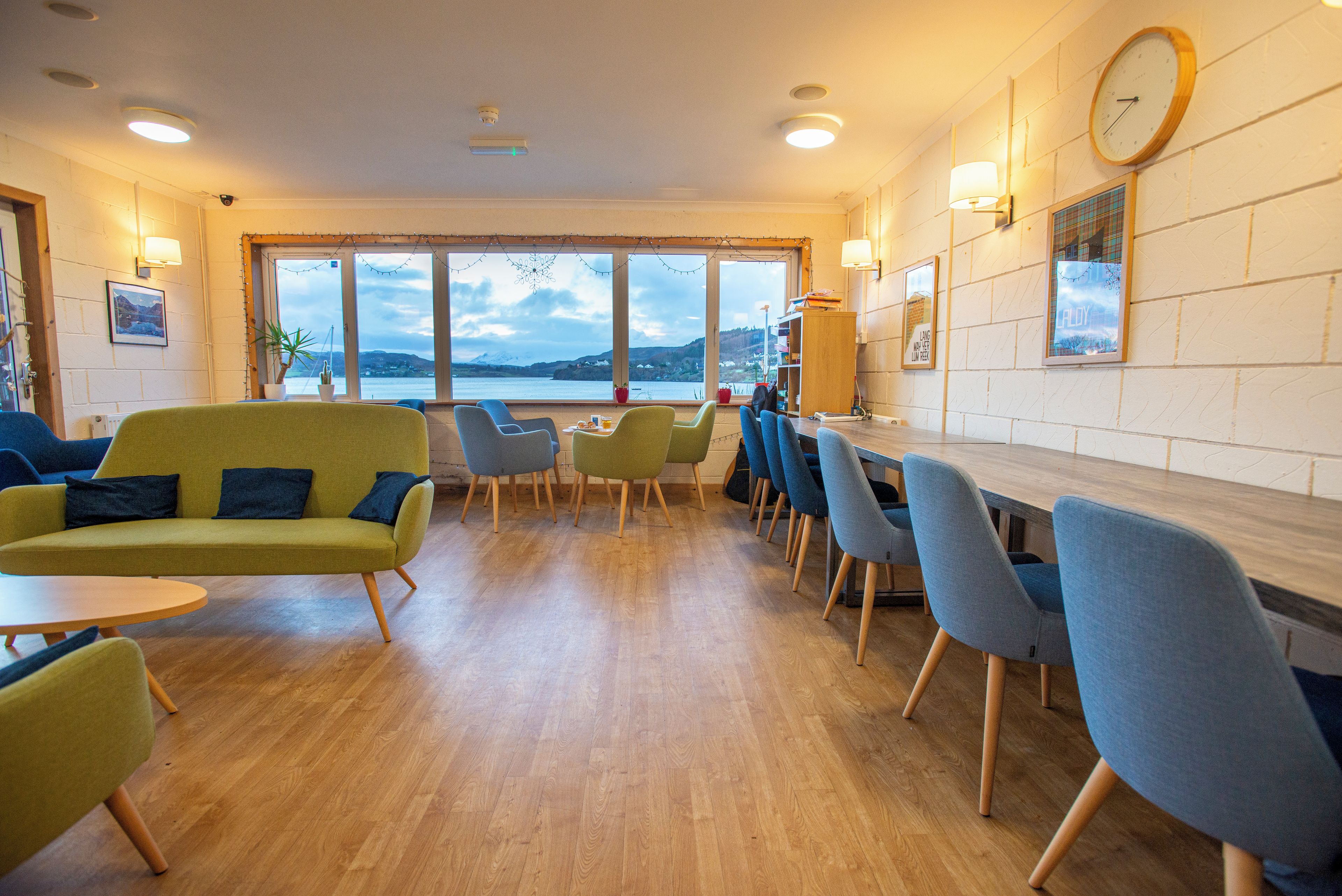 A modern interior with a wooden floor, a green sofa, blue chairs, and a view of the sea through large windows.