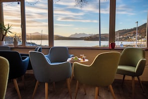 A seating area with chairs facing a large window overlooking a lake and mountains. - Portree Youth Hostel (Portree)