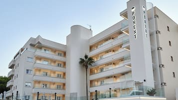 Een hotel met meerdere verdiepingen, modern van design, met balkons, een palmboom en een groot 'PONENT' bord.