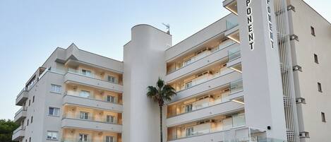 Een hotel met meerdere verdiepingen, modern van design, met balkons, een palmboom en een groot 'PONENT' bord.