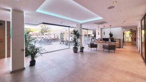 Un vestíbulo espacioso con diseño moderno, que cuenta con un mostrador de recepción, zona de estar y ventanas amplias con vistas al patio exterior.