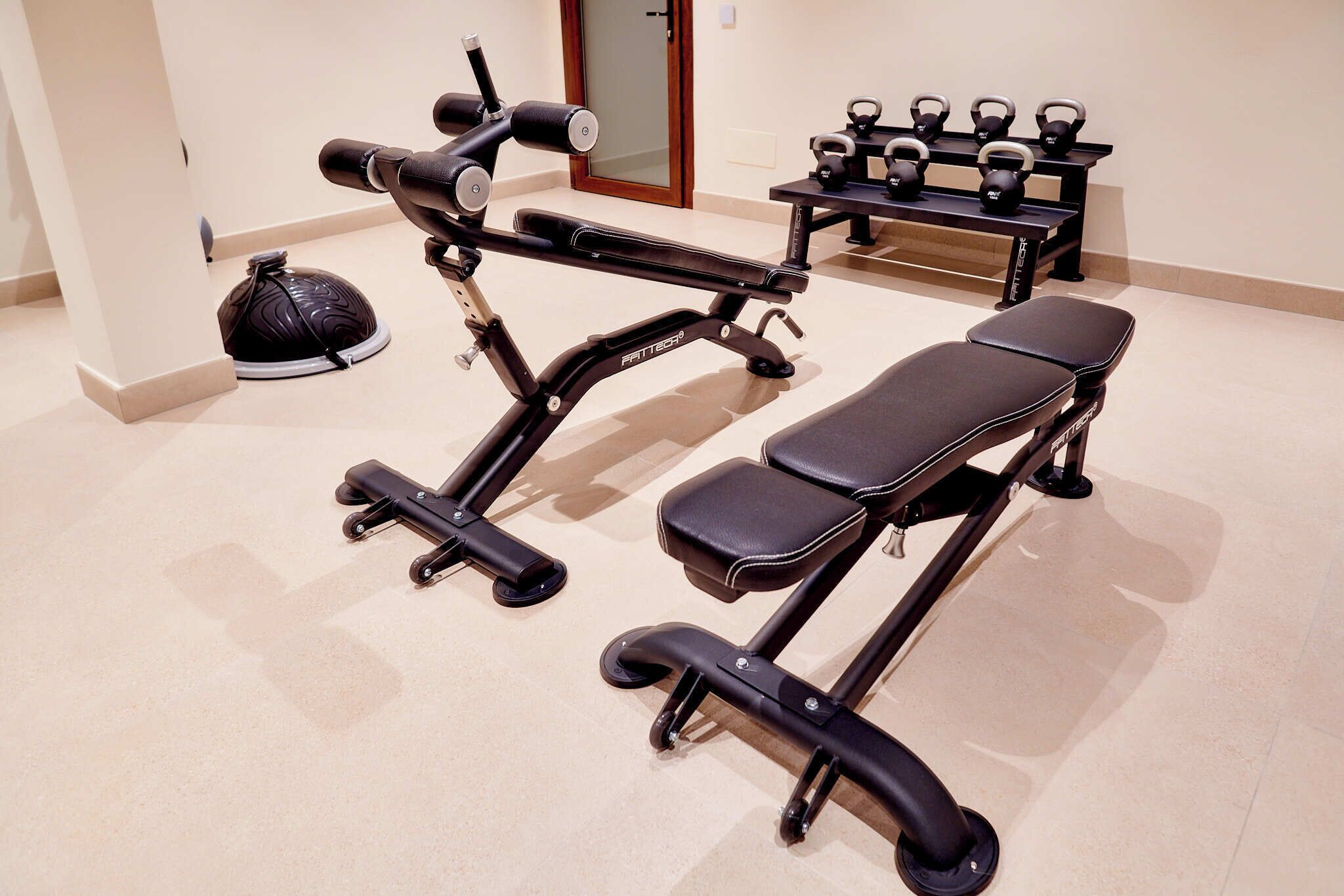 Un gimnasio con equipo de ejercicio, incluyendo una banca, mancuernas y una pesa rusa.