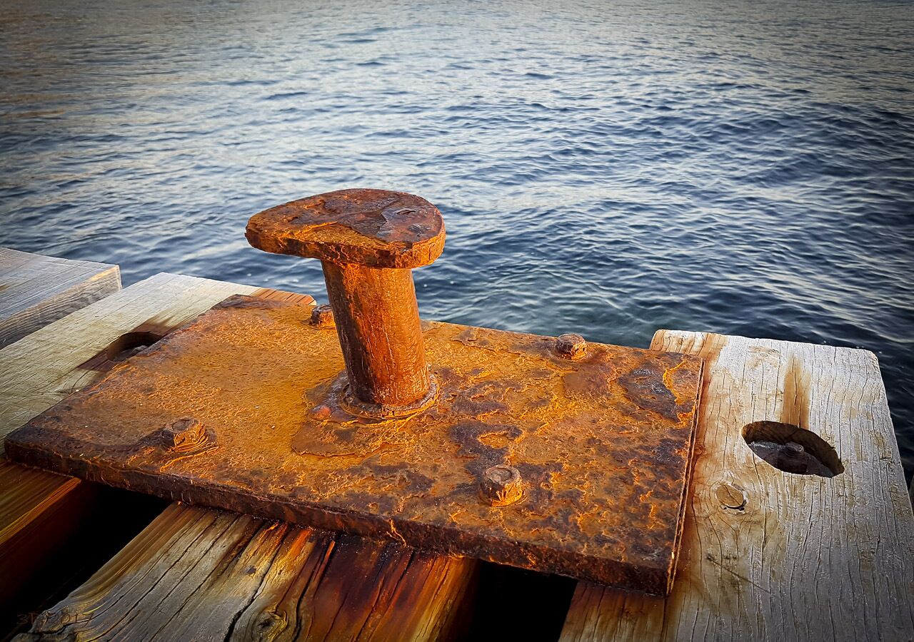 A rusted metal object on a wooden dock over water.