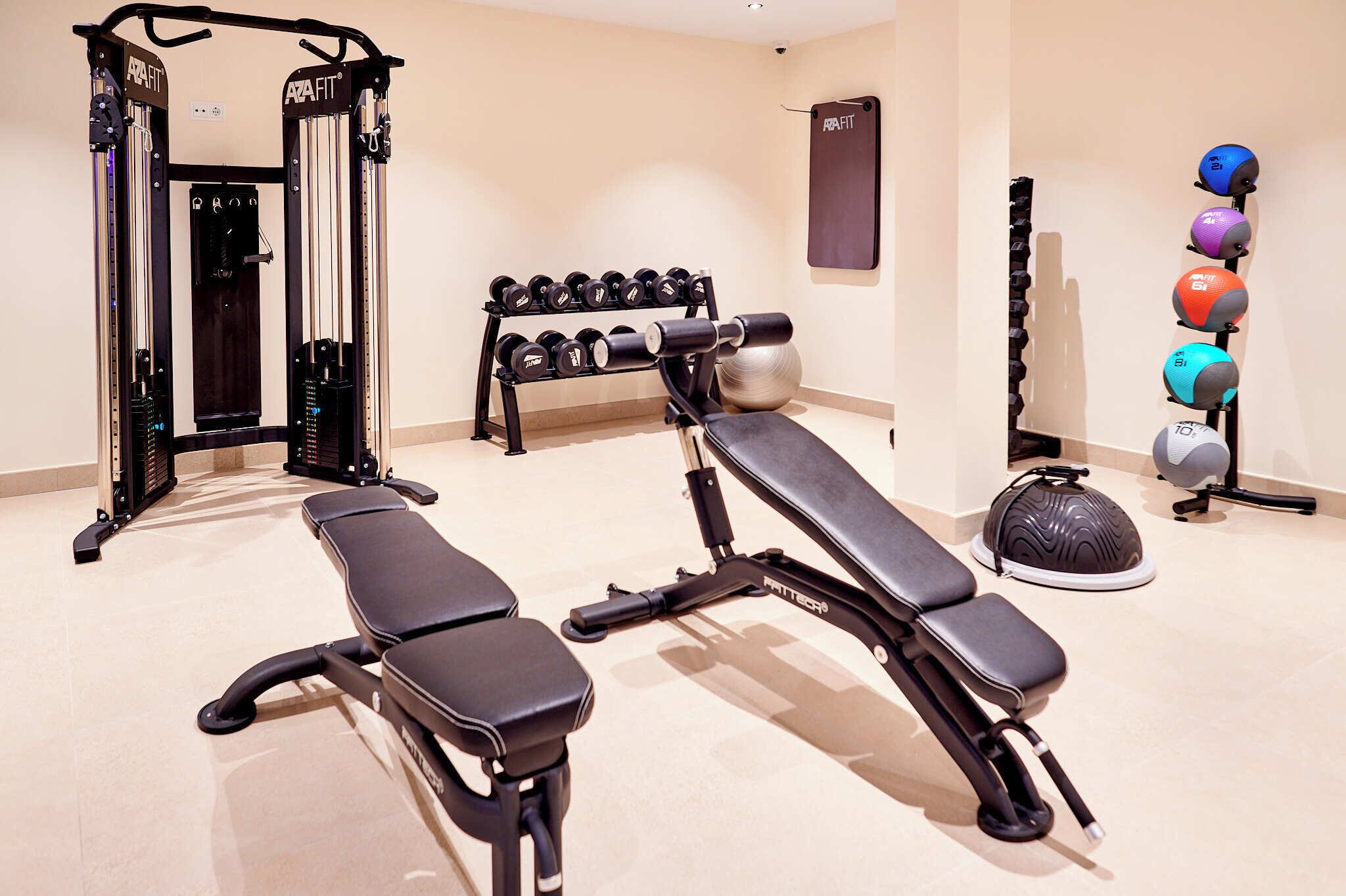Un gimnasio con una prensa de banca, mancuernas, un rack de sentadillas y pelotas de ejercicio.