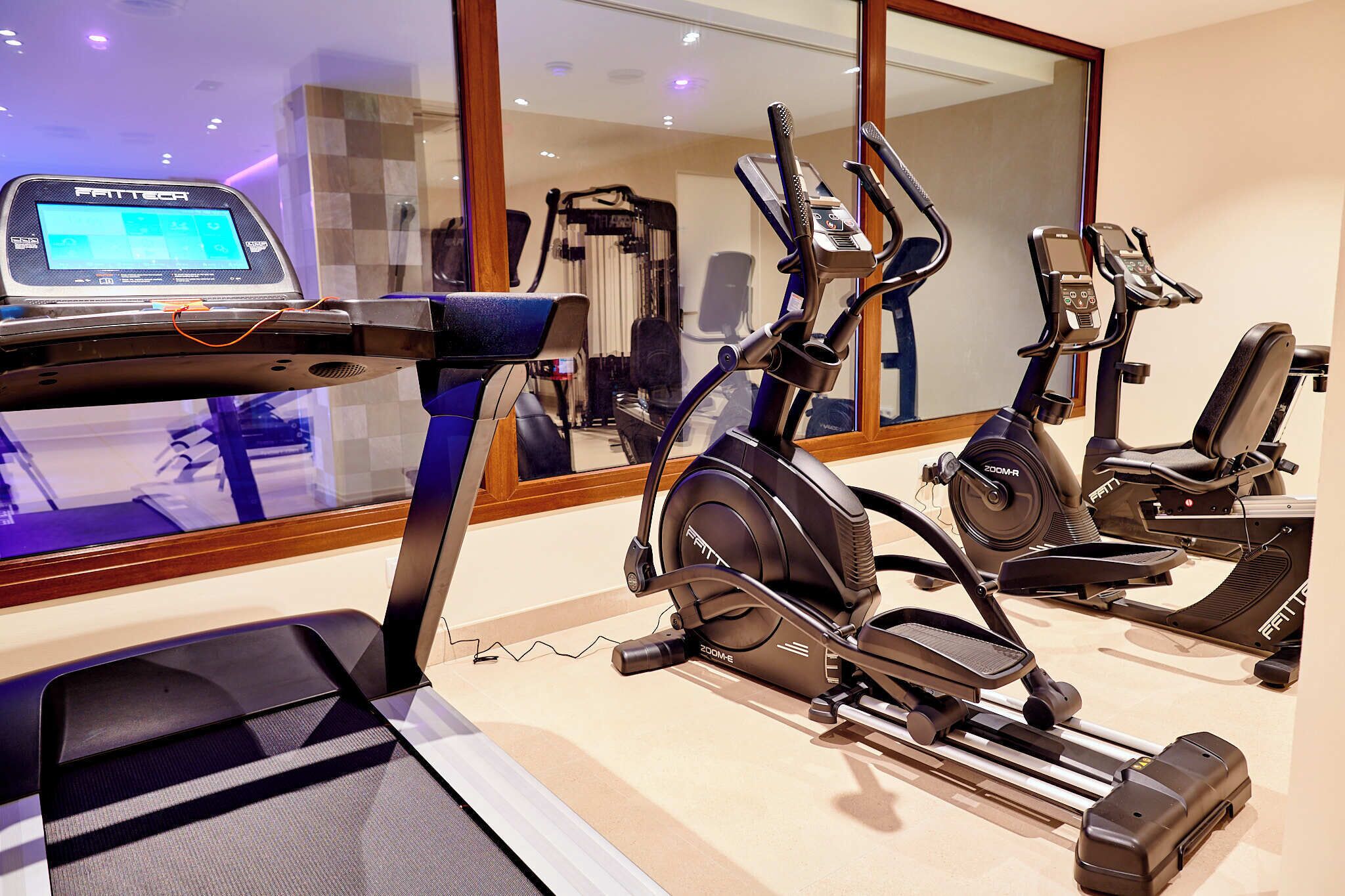 Een sportschool met hometrainers, een loopband en een digitale fitnessapparaat.